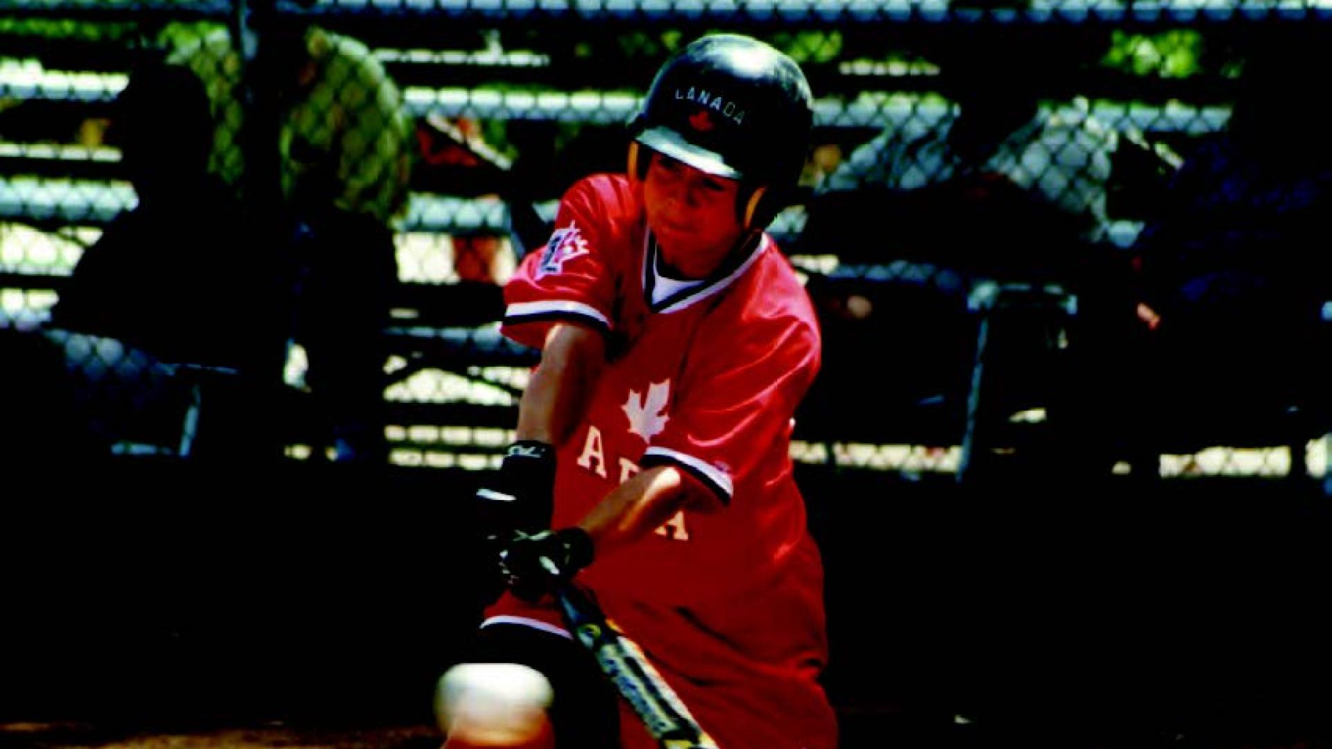 Leslie McPherson reaches out with a bat to hit a white ball approaching the base.